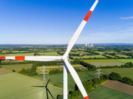 Windkraft Energie: Ein riesiger Windpark dominiert die Landschaft, umgeben von grünen Feldern und Bäumen. Im Hintergrund sind Kühltürme zu sehen.