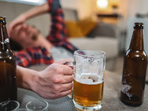 Mężczyzna leży na kanapie, trzymając kufel piwa. Wokół leżą puste butelki. Czy to oznacza, co przyspiesza spalanie alkoholu?