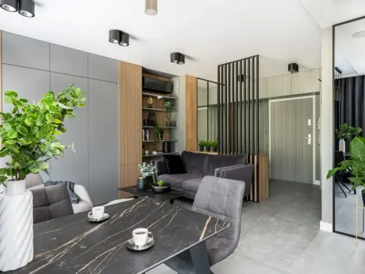 Nowoczesne mieszkanie 30m2 aranżacja: szara sofa, marmurowy stół, dużo zieleni i lustro.