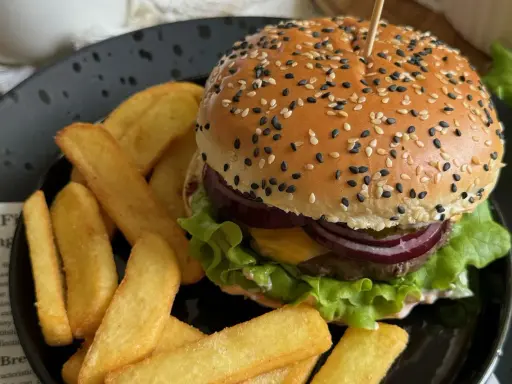 Soczysty burger wołowy z frytkami na czarnym talerzu.