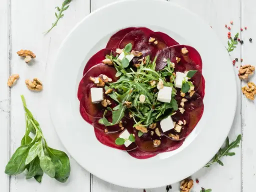 Rote Bete Carpaccio vegan mit Rucola, Walnüssen und veganem Feta auf weißem Teller.