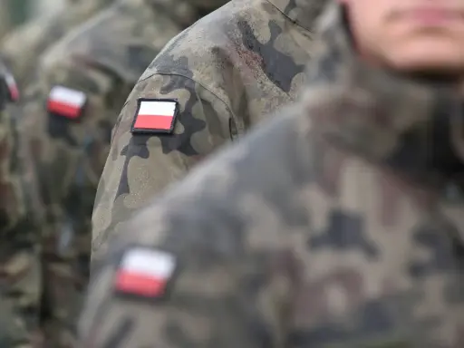 Żołnierze w mundurach moro, z polskimi flagami na ramionach, czekają na swoją emeryturę wojskową.