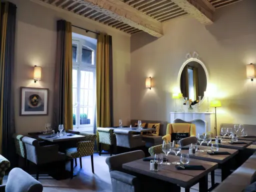 Salle à manger élégante avec tables dressées, fauteuils confortables et un miroir orné. L'ambiance évoque une **spécialité provençale** raffinée.