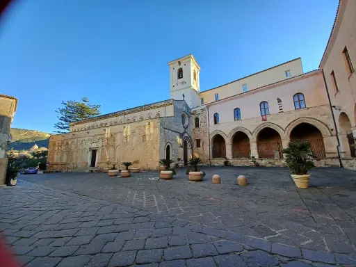 La piazza antistante la chiesa di Tropea, con il suo campanile e gli archi del chiostro, sotto un cielo azzurro.