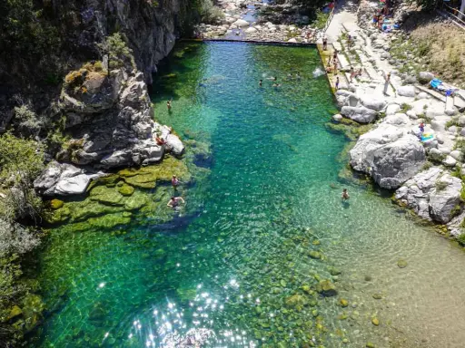 Una espectacular piscina natural en Extremadura, con aguas cristalinas y gente disfrutando del baño entre rocas y vegetación.
