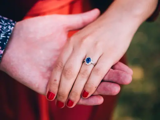 Dłoń z pierścionkiem z szafirem i diamentami, symbol miłości, jak szmaragd i szafir, w dłoniach pary.