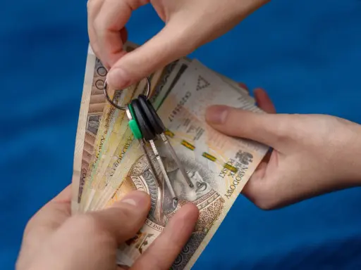 Dwie ręce trzymają plik banknotów i klucze. Zastanawiasz się, od jakiej kwoty płaci się podatek od wynajmu mieszkania?