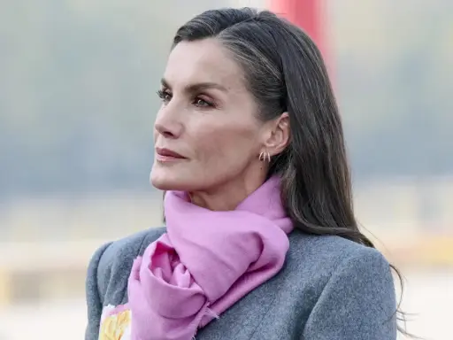 Mujer con elegante abrigo gris y bufanda rosa, su pelo sal y pimienta cae sobre sus hombros.