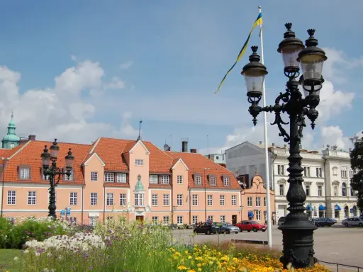 Blumen blühen am Karlskrona Hafen. Ein prächtiges Gebäude mit orangem Dach und eine schwedische Flagge im Wind.