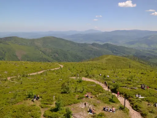 Malownicze widoki na Beskid Śląski, gdzie liczne istebne szlaki turystyczne prowadzą przez zielone wzgórza pełne jagód. Ludzie odpoczywają na trawie, ciesząc się słońcem.