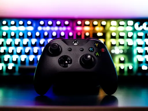 Czarny kontroler Xbox na tle podświetlanej klawiatury RGB. Idealny sprzęt do **grania na długie godziny**.