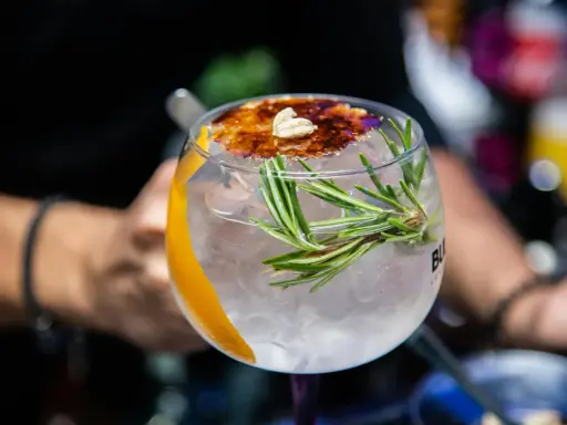 Ein erfrischender Gin Tonic, ein klassischer Cocktail, garniert mit Rosmarin, Orangenzeste und karamellisiertem Zucker.
