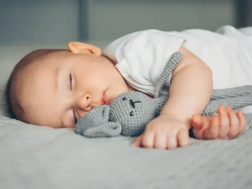Ein Baby schläft friedlich mit seinem Häschen-Spielzeug. Vielleicht ist es die berüchtigte 4 monats schlafregression, die es so müde macht.