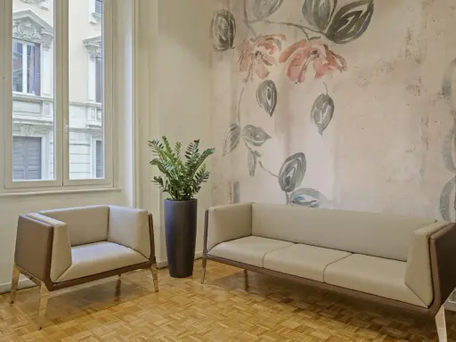 Eleganckie fotele i sofa na tle tapety z motywem kwiatowym. Czy można kleić tapetę na tapetę? Tutaj wygląda to stylowo.