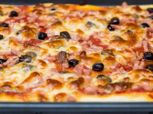 Une pizza rectangulaire garnie de jambon, d'olives et de fromage fondant. Parfait pour savoir que faire avec une pâte à pizza rectangulaire !