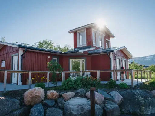 Rött hus med vita knutar och en solig veranda. Abisko Turiststation välkomnar besökare till fjällen.