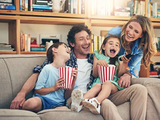 Rodzina śmieje się do rozpuku, jedząc popcorn podczas oglądania filmu dla całej rodziny.