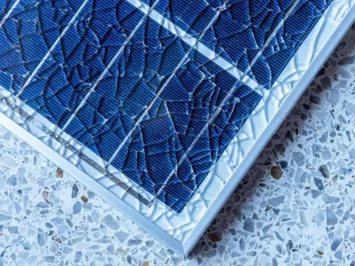 Gros plan sur un vitre panneau solaire brisé, ses fragments bleus reflétant la lumière sur un fond moucheté.