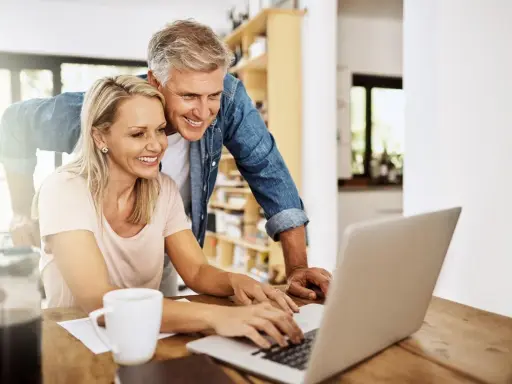 Uśmiechnięta para analizuje nowe przepisy dotyczące emerytur stażowych do końca roku na laptopie.