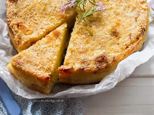 Delizioso gateau di patate dorato e croccante, guarnito con rosmarino fresco. Una fetta è già stata tagliata, invitando ad assaporare questo piatto saporito.