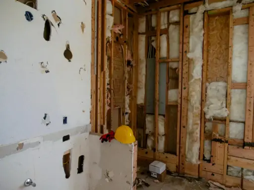 Chantier en cours, murs ouverts révélant l'isolant. Attention, la laine de bois peut présenter un danger si mal manipulée. Casque et gants de protection à proximité.