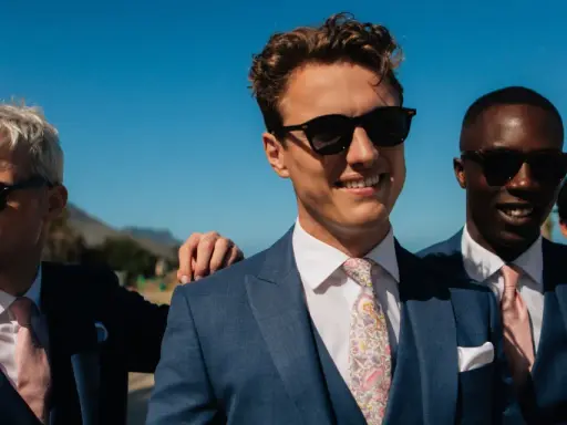 Four men in blue suits with pink ties and sunglasses, embodying a "dress to impress" dress code for a sunny outdoor event.
