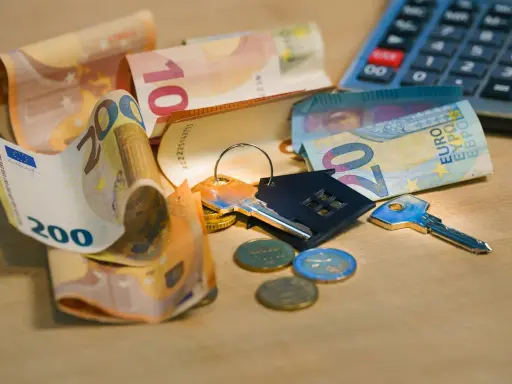 Clés, pièces et billets d'euros sur une table en bois. Calculatrice en arrière-plan. Le prix pose carrelage m2 est une préoccupation.