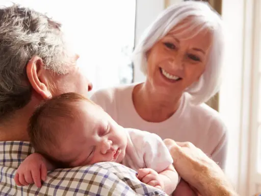 Los abuelos paternos sonríen mientras el abuelo sostiene al bebé dormido en su hombro.