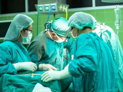 Zespół chirurgów w zielonych fartuchach i czepkach przeprowadza skomplikowaną operację głosu.