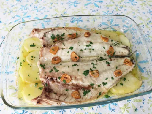 Lubina a la espalda horneada con patatas, ajo y perejil en una fuente de cristal.