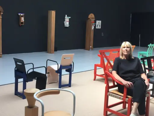 En kvinna sitter i en röd stol i en utställning med möbler av John Kandell.