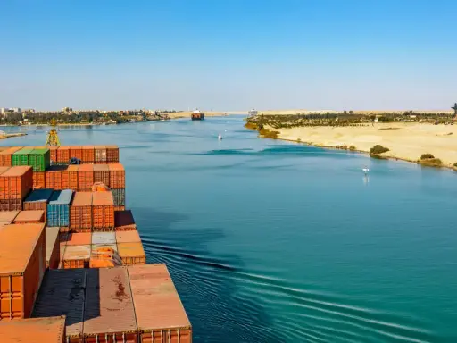 Containerrieschiff fährt durch den Suezkanal, ein Meisterwerk des Suezkanal Baus, vorbei an Wüstenlandschaft und Stadt.