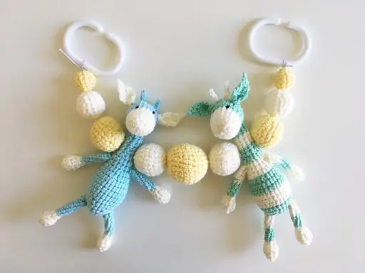 Crocheted giraffes with white and yellow beads hanging from white plastic rings.
