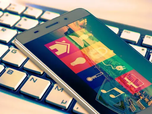 Smartphone mit Smart-Home-Symbolen auf Tastatur. Das Hacken Bedeutung wird hier durch die vielen Icons symbolisiert, die Zugang zu verschiedenen Bereichen des Lebens gewähren.