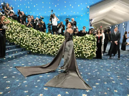 Kylie Jenner arrives at the Met Gala in a dramatic gown, posing for photographers amidst a sea of flowers and a blue, star-studded backdrop.