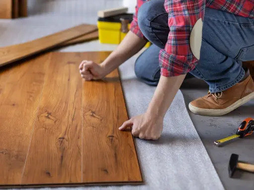 Persona posiziona assi di legno su un tappetino isolante, un passo fondamentale per come insonorizzare il pavimento e ridurre i rumori.