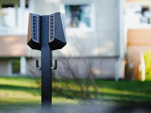 Svart laddstolpe Easee med krokar för laddkablar, placerad utomhus framför ett bostadshus.