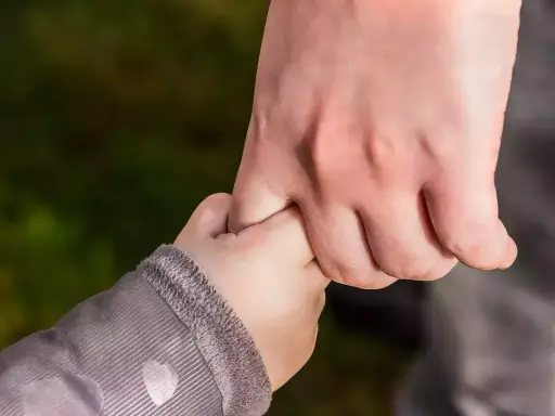 Dłoń dorosłego, opiekuna prawnego, mocno trzyma dłoń dziecka.