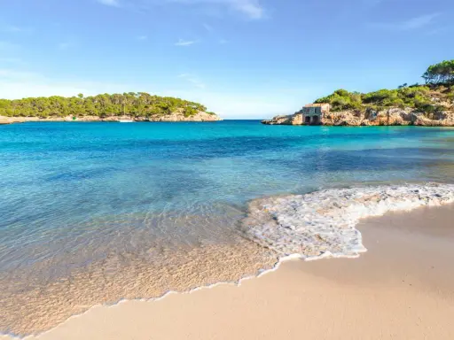 Türkisfarbenes Meer, Sandstrand und felsige Küste mit einem kleinen Haus auf Mallorca.