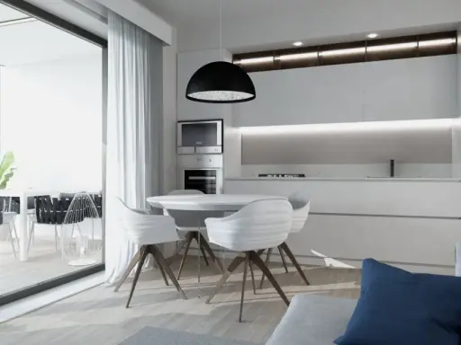 Interni luminosi di una casa di design con cucina moderna, tavolo rotondo e sedie bianche. Si intravede un terrazzo con piante.