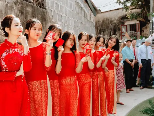 Novias y damas de honor con trajes rojos tradicionales, sosteniendo sobres rojos, celebrando una boda china.