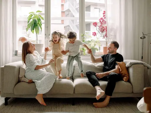Familjen hoppar glatt på soffan i detta hemma hos reportage. Barnen skrattar högt medan föräldrarna ler.