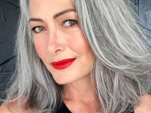 Donna con splendidi capelli grigi, labbra rosse vivaci e uno sguardo intenso.