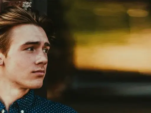 Junger Mann mit stylischen herren frisuren mittellang, lehnt an einer Ziegelwand.
