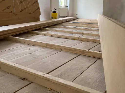 Holzbalken werden auf alten Dielen verlegt, um den Untergrund für einen neuen Dielenboden auszugleichen.