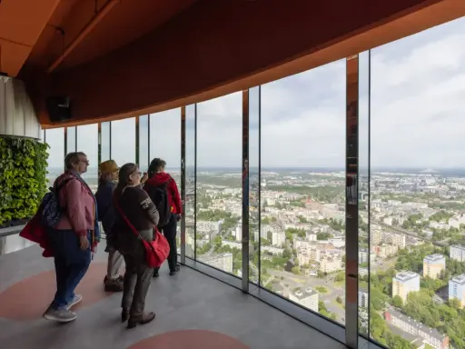 Grupa turystów podziwia panoramę miasta z tarasu widokowego najwyższego budynku we Wrocławiu.