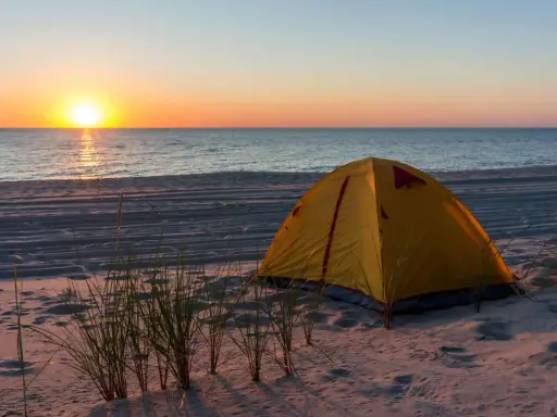 Żółty namiot na piaszczystej plaży, idealne miejsce na namioty z widokiem na zachód słońca nad morzem.
