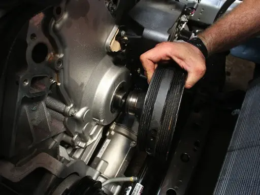 Mano retirando la polea del cigüeñal rota de un motor.