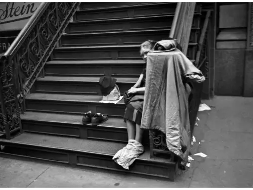 Una persona seduta sulle scale, con scarpe e cappello accanto. Un'immagine che evoca le cartier bresson foto famose, catturando un momento di vita urbana.