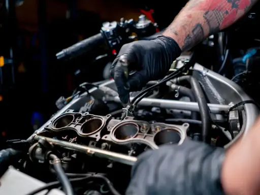 Mechanik w czarnej rękawiczce pracuje przy silniku motocykla, regulując elementy układu chłodzenia.